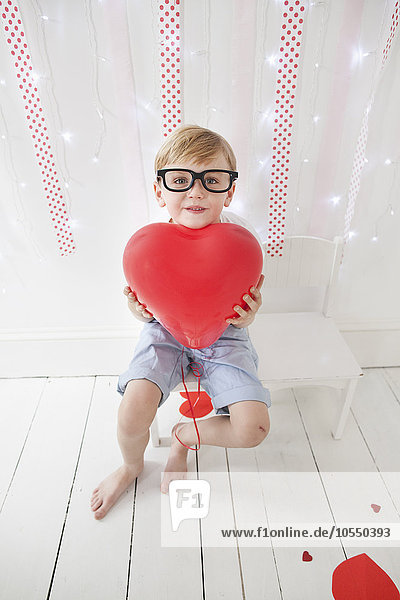 Young boy posing for a picture in a photographers studio  holding red balloons.