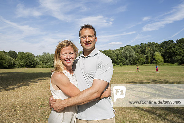 Ein Paar steht in einem Park  lächelt und umarmt sich.