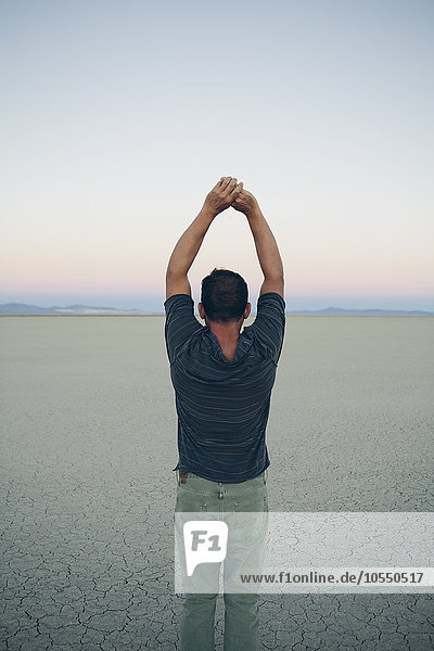 Mann streckt die Arme über den Kopf und blickt auf den Sonnenaufgang über der ausgedehnten Wüste  Black Rock Desert  Nevada