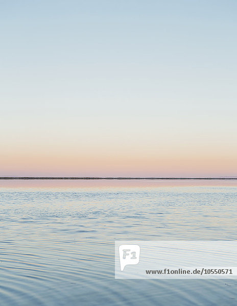 Der Blick auf die klare Linie des Horizonts  wo Land auf Himmel trifft  über die überflutete Fläche der Bonneville Salt Flats. Das Licht der Morgendämmerung