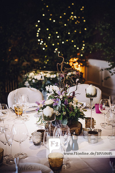 Ein für einen besonderen Anlass gedeckter Tisch  mit einem floralen Tafelaufsatz und Kerzen  bei Nacht.
