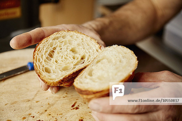 Ein Mann hält ein in zwei Hälften geschnittenes Croissant in der Hand  um die leicht geschichtete Textur des gekochten Teigs zu zeigen.