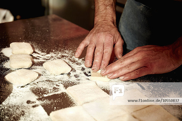 Ein Bäcker,  der auf einer bemehlten Oberfläche arbeitet und den vorbereiteten Teig in Quadrate teilt.
