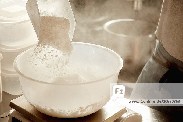 Ein Bäcker  der Zutaten vorbereitet  eine Messskala verwendet und Mehl in eine Schüssel gießt.