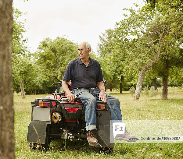 Ein Bauer sitzt auf dem Rücken eines Quad-Fahrrads auf einem Feld und vermisst sein Land und seine Tiere.