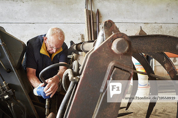 A man working with tools on farm machinery in a barn.