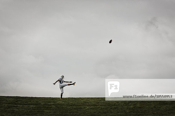 Ein Fußballspieler in Uniform  Seitenansicht  der sein Schießen übt. Ball in der Luft.