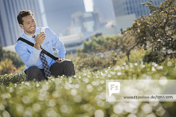 Ein junger Mann auf einer Parkbank in der Stadt  der ein Mobiltelefon benutzt.