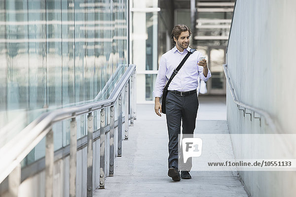 Ein Mann trägt eine Computertasche mit einem Gurt über der Brust auf einem Bürgersteig in der Stadt.