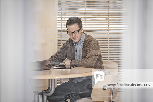 Ein Mann  der an einem Tisch sitzt und ein digitales Tablett benutzt.