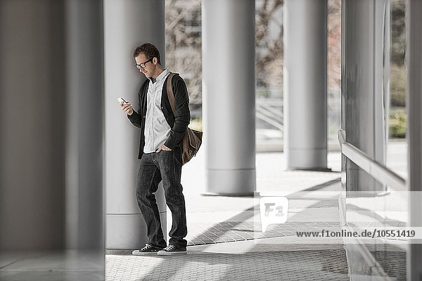 Ein Mann vor einem Gebäude  der sein Smartphone überprüft.