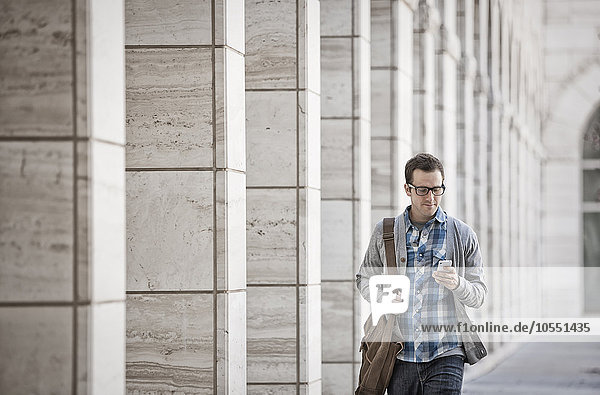 A man outside a building  checking his smart phone.