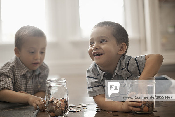 Zwei Kinder spielen mit Münzen  indem sie diese in Glasgefäße fallen lassen.