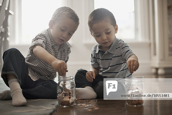 Zwei Kinder spielen mit Münzen  indem sie diese in Glasgefäße fallen lassen.