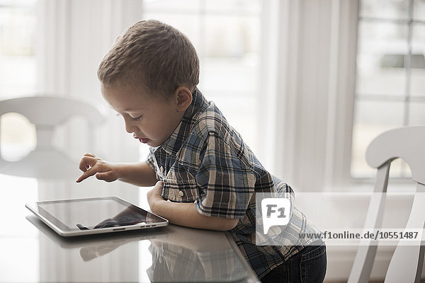 Ein Kleinkind  das an einem Tisch sitzt und ein digitales Tablett mit einem Touchscreen benutzt.
