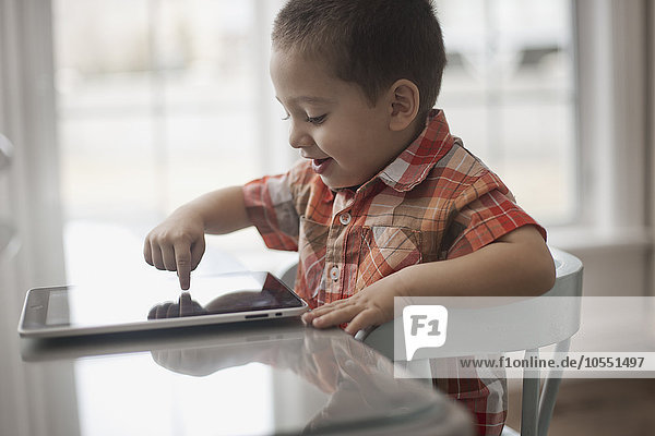 A young child sitting at a table using a digital tablet with a touchscreen.