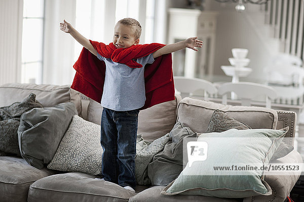 Ein Kind steht mit einem roten Umhang  die Arme in Superheldenpose erhoben.