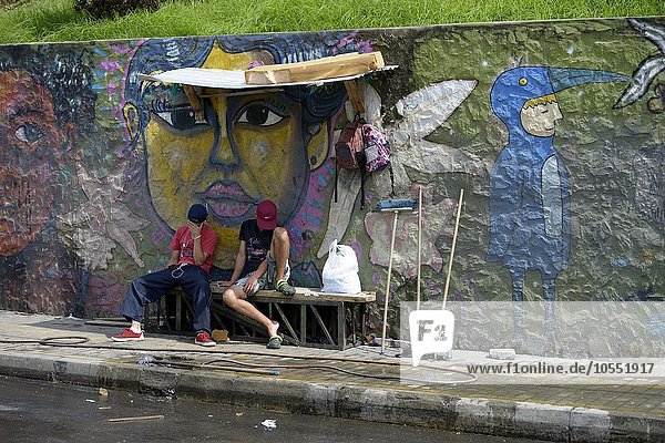 Jugendliche Bandenmitglieder sitzen vor einer mit Graffiti besprühten Mauer  Armenviertel Comuna 8  Medellin  Departamento Antioquia  Kolumbien  Südamerika