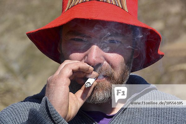 Man with red hat and beard smoking cigarette