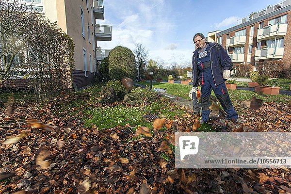 Hausmeister mit Laubbläser wirbelt in einer Wohnsiedlung Blätter auf  Hausmeister-Service  Deutschland  Europa