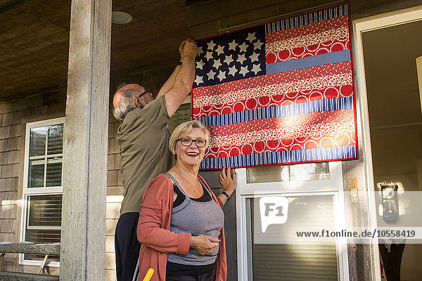 Kaukasisches Paar hängt selbstgemachte amerikanische Flagge auf Veranda