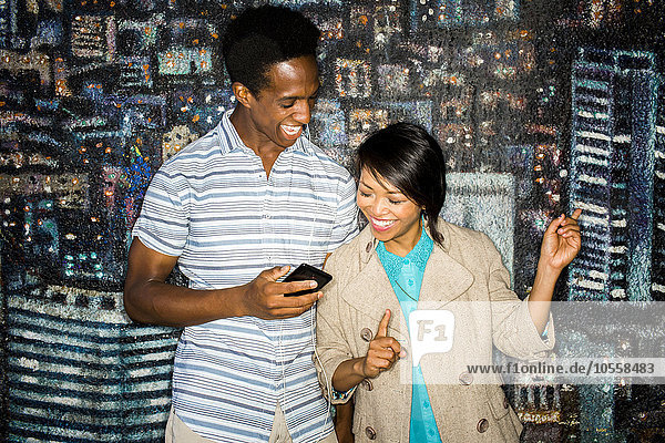 Ehepaar benutzt Handy vor Wandmalerei