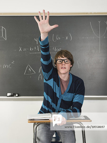 Schüler hebt seine Hand am Schreibtisch im Klassenzimmer