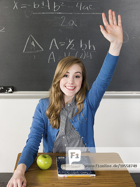 Schülerin hebt ihre Hand am Schreibtisch im Klassenzimmer