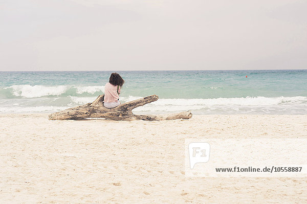 Frau sonnt sich auf einem Treibholzstamm am Strand