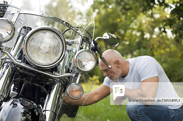 Älterer Mann repariert Motorrad im Park
