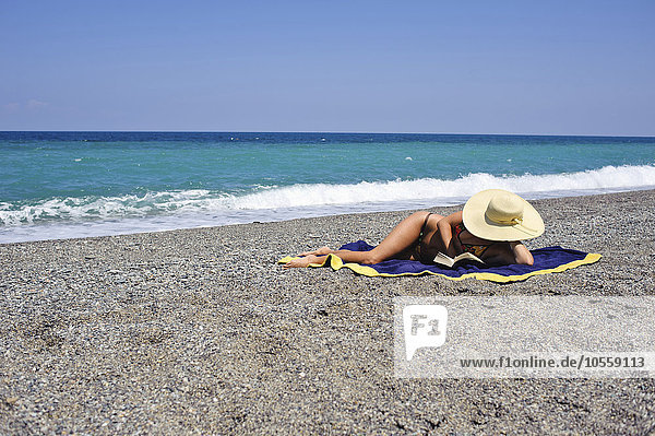 Frau beim Sonnenbaden und Lesen am Strand