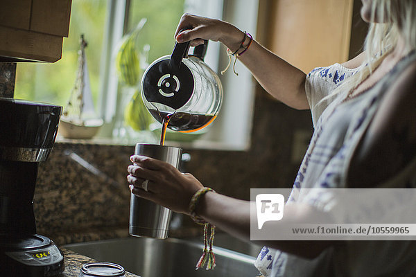 Kaukasische Frau gießt in der Küche eine Tasse Kaffee ein