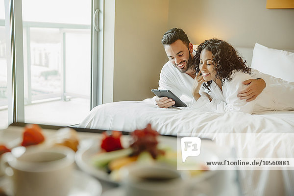 Ehepaar benutzt digitales Tablet auf dem Hotelbett