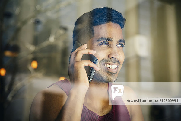 Indischer Mann  der in einem Café mit seinem Handy telefoniert