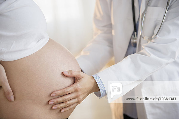 Arzt untersucht den Bauch einer schwangeren Frau