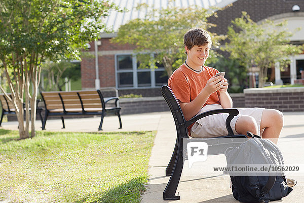 Caucasian teenage boy using cell phone on bench