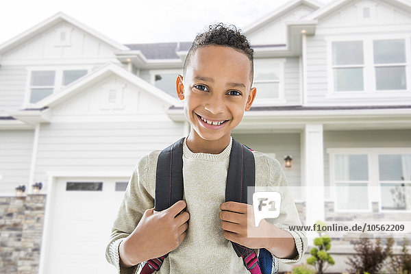 Schwarzer Junge mit Rucksack lächelt vor dem Haus