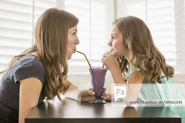 Caucasian mother and daughter sharing milkshake