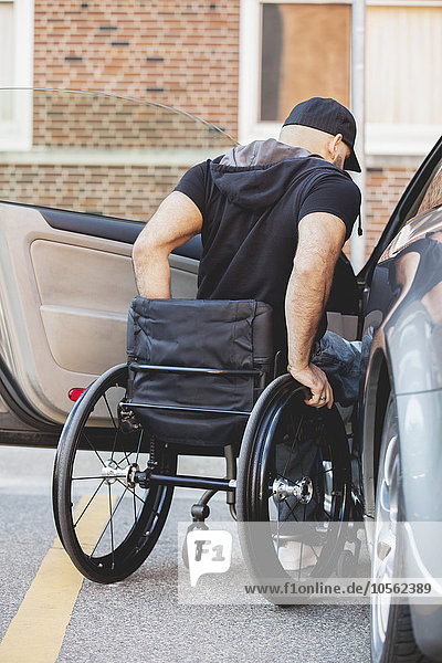 Behinderter Mann im Rollstuhl klettert ins Auto