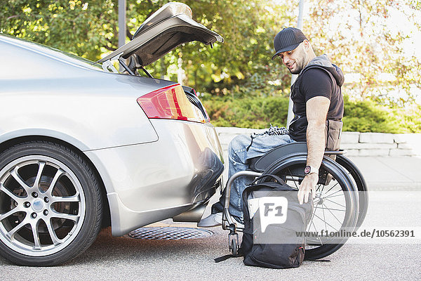 Behinderter Mann im Rollstuhl packt Autokofferraum
