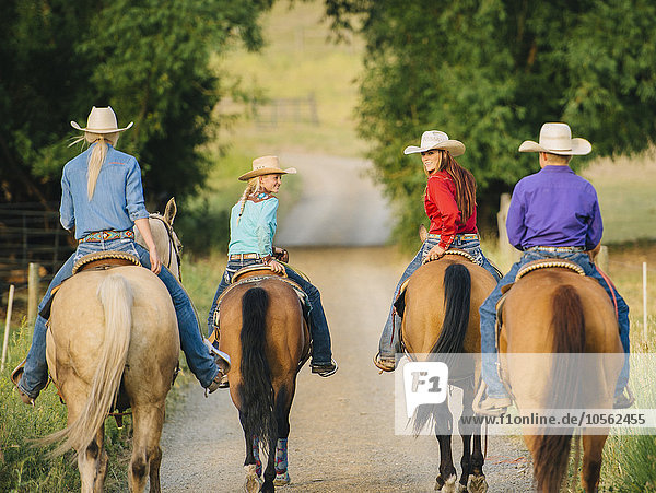 Cowgirls und Cowboy reiten auf Pferden auf einer Landstraße