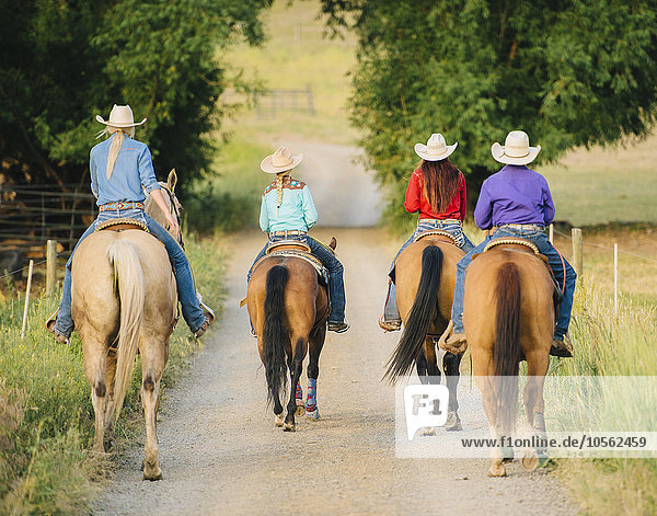 Cowgirls and cowboy riding horses in rural road