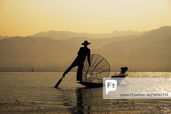 Asiatischer Fischer rudert Kanu auf ländlichem See