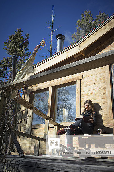 Weiße Frau liest ein Buch auf der Veranda einer Hütte