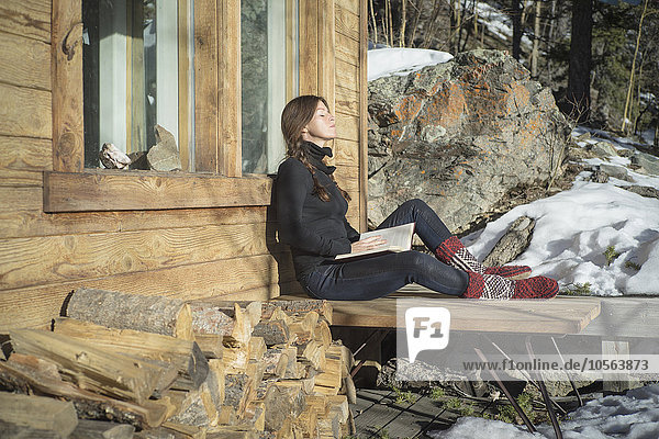 Weiße Frau liest ein Buch auf der Veranda einer Hütte