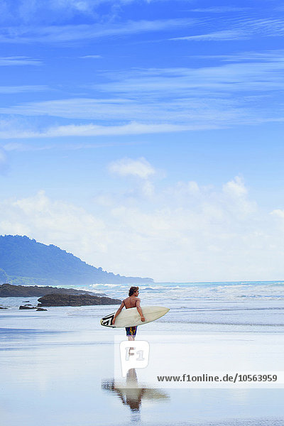 Mann trägt Surfbrett am Strand