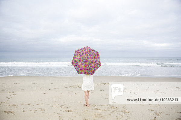 Frau mit Sonnenschirm am Strand stehend