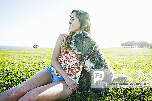 Kaukasische Frau sitzt mit Hund auf einem Feld