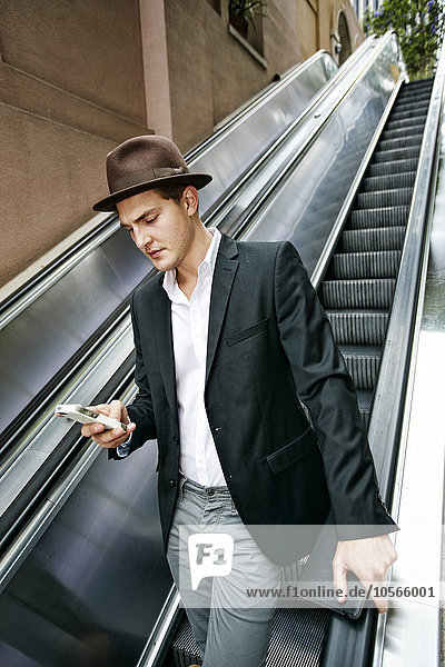 Kaukasischer Geschäftsmann benutzt Mobiltelefon auf Rolltreppe
