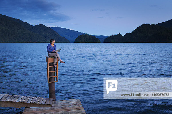 Japanische Frau sitzt auf einem Holzsteg am See